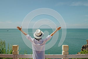 Asian woman standing relax on cliff, She looking forward to sea and raised hers hand over head.