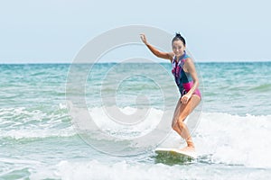 Asian woman standing on a surfboard smiling happy from the surf which is exercise
