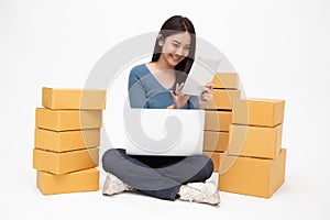 Asian woman startup small business freelance holding tablet and computer laptop and sitting on floor with parcel box