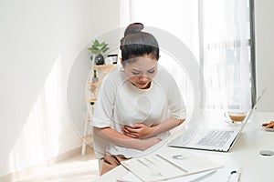 Asian woman with stomach ache or feeling hurting stomach in office table