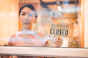 Asian woman store owner turning hanging closed sign