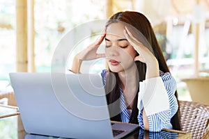 Asian woman with stressed back working in front of one laptop computer on front desk. with a stern expression, rubbing his head