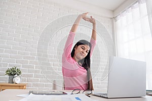 Asian woman stretching arm up when working on laptop at white br