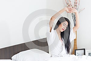 Asian Woman stretching in bed with her arms raised