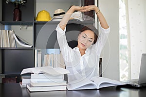 Asian woman stretching at her workplace and smiling in the office