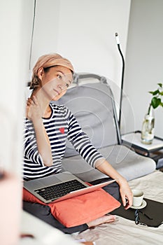 Asian woman stretching nec on bed during working from home on laptop