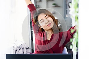 Asian woman stretching and raised arms  taking a break and relaxing while working on laptop
