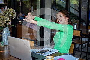 Asian woman stretching after reading book and work hard and smiling in coffee shop