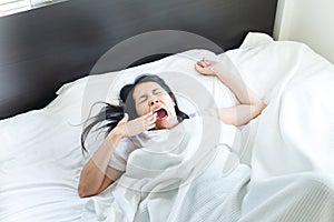 Asian woman stretching and yawning or gape feeling lazy on bed after wake up in the morning