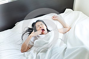 Asian woman stretching and yawning or gape feeling lazy on bed after wake up in the morning photo