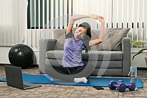 Asian woman stretching during a yoga class with a trainer at her laptop computer at home