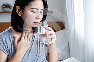 Asian woman suffering from sore throat drinking a glass of warm water in the morning