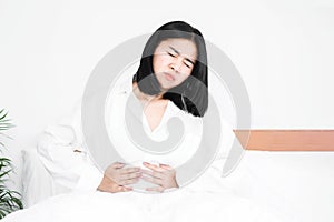 Asian woman suffering from stomach ache,  sitting in bed