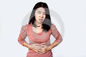 Asian woman suffering from stomach pain hand holding her tummy isolated over grey background