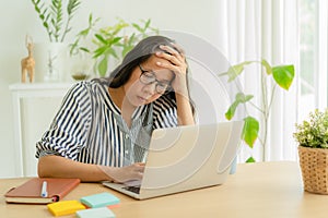 Asian woman suffering stress working on laptop in overworked. Tired businesswomen using computer and holding her hand on her templ