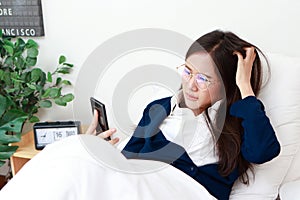 Asian woman in suit lying on bed holding smartphone online chatting work She has stress.