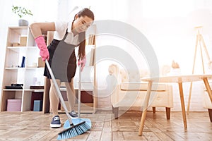 Asian woman sweeps floor while standing in room.