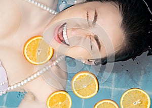 Asian woman is swimming with a slice of orange floating above the water in a blue pool