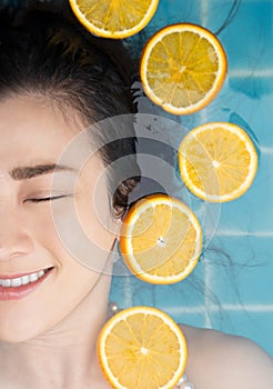 Asian woman is swimming with a slice of orange floating above the water in a blue pool