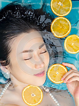 Asian woman is swimming with a slice of orange floating above the water in a blue pool