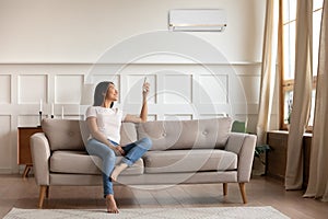 Asian woman switching on air conditioner while resting seated indoors