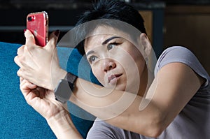 Asian woman takes a picture selfy on red phone lying on blue pillow