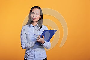 Asian woman taking notes on blue clipboard with pen