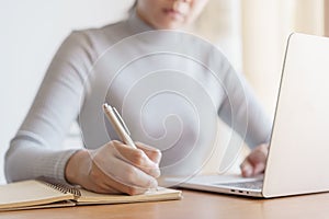 Asian woman is taking notes and using  laptop computer at office photo