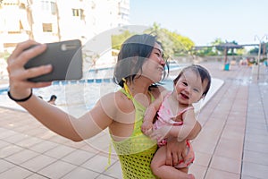 Asian woman taking selfie photo with her adorable baby girl - beautiful Chinese mother holding her little daughter and taking