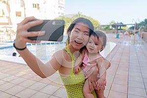 Asian woman taking selfie photo with her adorable baby girl - beautiful Chinese mother holding her little daughter and taking