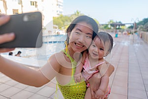 Asian woman taking selfie photo with her adorable baby girl - beautiful Chinese mother holding her little daughter and taking