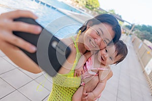 Asian woman taking selfie photo with her adorable baby girl - beautiful Chinese mother holding her little daughter and taking