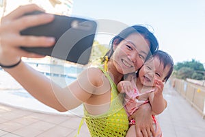 Asian woman taking selfie photo with her adorable baby girl - beautiful Chinese mother holding her little daughter and taking