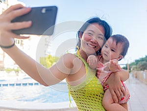 Asian woman taking selfie photo with her adorable baby girl - beautiful Chinese mother holding her little daughter and taking