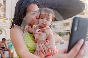 Asian woman taking selfie photo with her adorable baby girl - beautiful Chinese mother holding her little daughter and taking