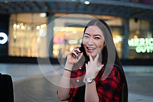 Asian woman talking on mobile phone while standing at outdoor shopping mall in the evening.