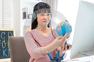 Asian woman teacher teaching geography via video conference e-learning and cheerful elementary school student looking at globe,