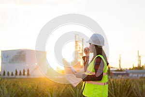 Asian woman technician Industrial engineer using walkie-talkie and holding bluprint working in oil refinery for building site