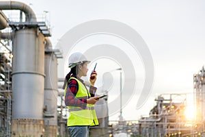 Asian woman technician Industrial engineer using walkie-talkie and holding bluprint working in oil refinery for building site