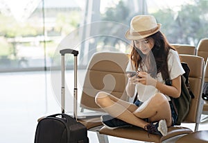 Asian woman teenager using smartphone at airport terminal sitting with luggage suitcase and backpack for travel in vacation summer