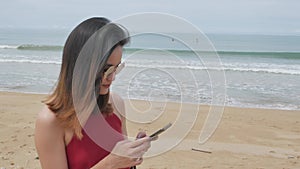 asian woman texting mobile phone while walking on the white sand beach