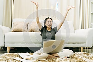 Asian woman throws papers in the living room as she finishes her work with her laptop on her lap