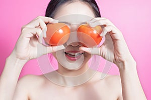 Asian woman with tomato concept. She smiling and holding tomato. Beauty face and natural makeup. Isolated over pink background.