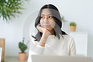 Asian woman touching chin and looking outside the window using laptop, computer , working at home. Asia student happy smile. Close