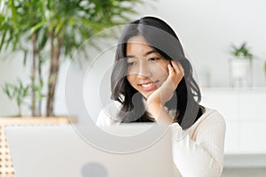 Asian woman touching chin and using laptop, computer , working at home. Asia student happy smile. Close- up on girl face