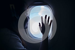 Asian woman touching and looking through an airplane window with clouds and sky background