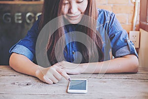 Asian woman touching and using smart phone with feeling happy while sitting in vintage wooden cafe