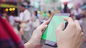 Asian woman tourist backpacker smiling and using green screen smartphone traveling alone holidays outdoors on city street.