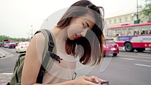 Asian woman tourist backpacker smiling and using smartphone traveling alone holidays outdoors on city street in Bangkok - Thailand