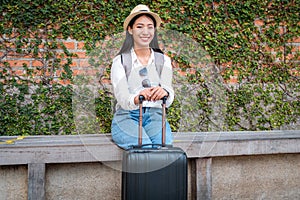 Asian woman tourist sitting on the chair with hat and holding her luggage to preparing on holiday